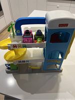 Photo of Fisher Price Little People Parking Garage showing three levels with spiral ramp on left, elevator with door on right, and two small Little People vehicles parked on upper level.