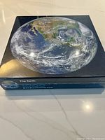 Photo of the puzzle box showing the Earth from a US West Coast perspective with visible cloud patterns and continents.