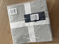 Folded grey knit blanket with a white ribbon and two tags with barcode and brand information visible, showing the new condition.