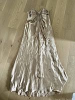 Full view of the champagne silk gown laid flat on a wooden floor, showing its length and pleated bodice detail.