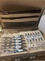 Top view of briefcase open revealing six serrated knives and six forks secured inside with protective plastic and labels attached.