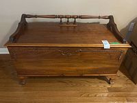 Front view of the antique cedar lined wood chest showing the carved detailing and handle on the front panel along with the decorative wooden rail top.