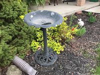 Full view of bird bath showing flower-shaped basin and cast iron stand, set outdoors in garden mulch and plants.