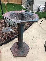Full view of the iron bird bath showing textured basin, post, and base on outdoor patio.