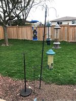 Image of bird feeders on two metal garden hook stands set outdoors in a yard with a wooden fence in the background.