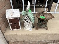 Full view of two wooden birdhouses and one cast iron pagoda candle lantern on a porch step.