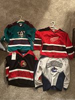 Four children's hockey jerseys displayed on carpet showing team logos and colors