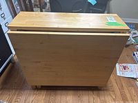 Table in folded position showing wooden surface and drop leaves.