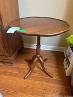 Side angle view showing the scalloped edges of the wood top and the turned pedestal base with four legs.