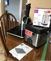 Four kitchen appliances placed on a wooden chair, showing Dalton induction cooktop, Yonanas frozen banana maker, Salton fryer and hotplate, T-fal fryer and the induction cooktop manual.