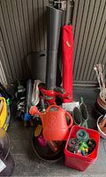 Photo showing watering can, Toro blower/vac tube, red container with garden sprinkler accessories, green boots, and various tools.
