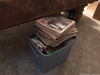 Stack of hockey magazines piled on top of a blue-gray plastic tote bin, showing multiple issues and covers.