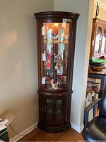 Front view of the lighted corner curio cabinet in a room corner with various collectibles inside.