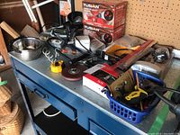 Wide view of lot items on a blue workbench including measuring tape, pet bowls, tools, and boxes of Fusion Galaxy Lights