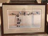 Full view of the framed lithograph print showing a young hockey player in jersey 19 facing several players on a bench wearing helmets and gloves.