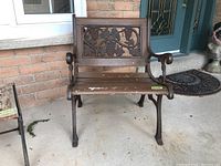 Front view of a wood and cast iron outdoor bench chair with grapevine design on the backrest and visible weathering, scratches, and paint chipping on wooden slats.