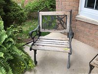 Front view of wooden slat bench chair with cast iron arms and legs, showing the decorative nature of the backrest panel and the overall weathered condition.