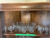 Multiple pinwheel cut crystal brandy snifters and short tumblers arranged on wooden shelf