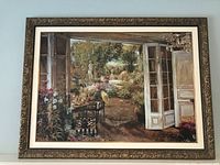 Framed print on canvas depicting garden scene with open doors, table, chairs, and flowers.