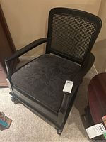 Full view of the rocking armchair showing black wooden frame, wicker backrest, and floral patterned black cushion seat.