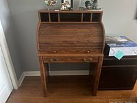 Front view of the wood roll top desk with contents on top, tambour cover closed, drawer closed.