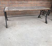 Full view of long rectangular outdoor table with weathered wooden slat top and cast iron legs on concrete surface against brick wall