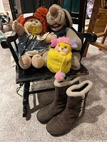 Front view of the Cabbage Patch doll with the pacifier, the two animal toys on a black wooden chair, and the brown boots in front.