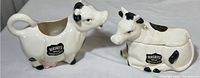 Pair of vintage ceramic Hershey's Milk Chocolate cow dishes: the creamer and sugar dishes side by side, showing logo decals and cow shape.