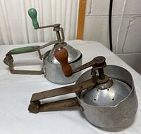 Pair of two vintage metal manual juicers with wood handles, positioned side by side showing general form and condition.