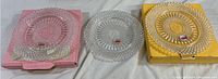 Three clear crystal Avon plates displayed on original colored boxes (pink and yellow) showing detailed faceted cuts.