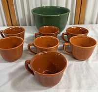 Photo of seven brown pottery cups grouped on white cloth, showing shape and color