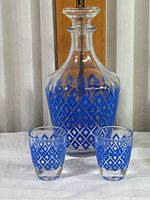 Front view of clear glass decanter and two matching glasses with blue diamond pattern.
