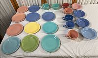 Overview of all colorful pottery plates and cups on white surface, showing multiple plates in various pastel colors and several cups.