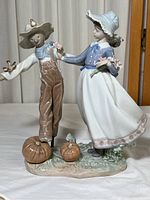 Front view of glossy porcelain figurine of scarecrow and girl, with pumpkins at base, showing size and color.