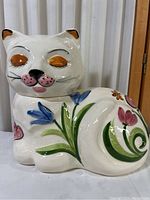 Side view of white cat cookie jar showing floral painted design and eye detail.