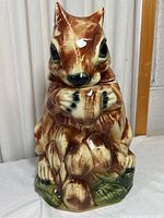 Front view of the squirrel-shaped ceramic cookie jar showing the face, ears, paws holding an acorn, and the grassy base.