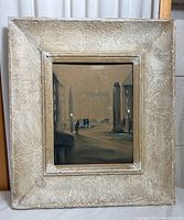 Front view of original small painting in ornate textured frame showing nighttime street scene with car and buildings.