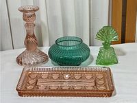 Full view of four glass items: pink candlestick, green bowl, green perfume bottle, pink glass tray.