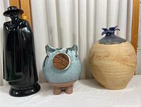 Photo of all three pieces: black figurine, owl vase, and beige flower pot on a table with curtain background.