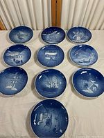 Set of ten blue and white porcelain plates arranged in a 3-3-3-1 pattern showing various winter, holiday, and village scenes.