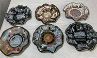 Six vintage American glass ashtrays displayed on a white surface showing various historic and landmark designs.