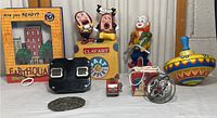 Wide view of lot showing multiple vintage toys including clown figure on unicycle, Earthquake toy, Clayart figurines, spinning top, fire truck, metal decorative item, toy wheel and small boxed item