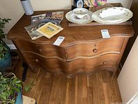 Front angle view of the antique wooden dresser showing three drawers and wooden knobs, placed on hardwood floor with some decorative items on top.