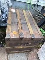 Top view of antique wooden steamer trunk with iron bands and aged wood surface, showing label and wear.