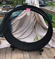 Side view of the large black rotating cat exercise wheel resting on a deck with a white cloth background, showing the full circular shape and the sticker label on the top.