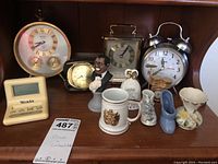 Front view of the lot displaying four clocks, a Louis Armstrong bust, a miniature stein, shoe figurines, and bell on a wooden shelf.