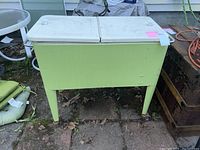 Front view of the pale green standing chest cooler outdoors on a patio with two white hinged lids closed.
