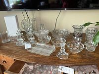 Several crystal and glass items displayed on a wooden surface. Includes bowls, candle holder, pitcher, vase, glasses, and a divided dish.