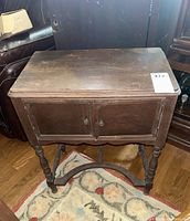 Closed dark wooden humidor cabinet showing rectangular top, two doors, and spindle turned legs with curved stretcher base.