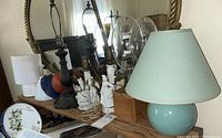 Lot of various lamps and Victorian figurines on a wooden surface with mirror background.